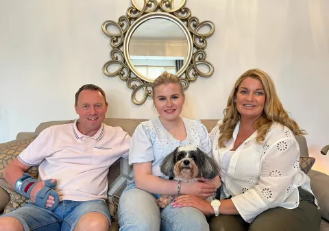 Stuart, Lucy and her mum sit on the sofa smiling with their dog