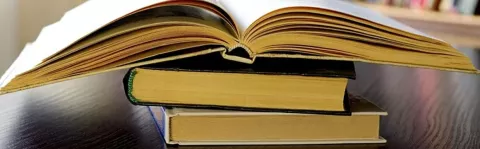 The photo shows three books stacked on top of each other with the top one lying open