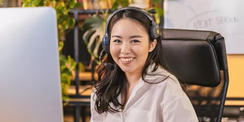 Woman wearing headset smiles to camera from behind computer screen