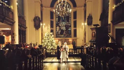 The photo shows the inside of the church lit by candlelight with an audience sitting in the pews
