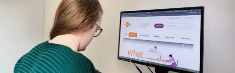 A woman with progressive MS sits at her desktop computer looking at the MS Society website