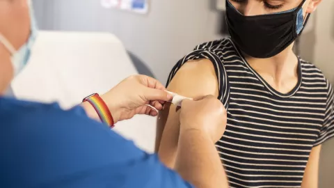 A person sticks a plaster on another person's arm after receiving an injection