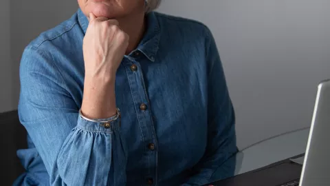 A cropped image of a woman resting her chin on her closed hand as she sits at a computer