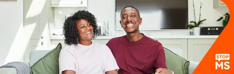 Nikoma and Simone on their sofa at home holding each other and smiling