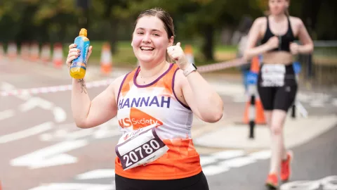 A woman taking part in a charity run, giving a thumbs up