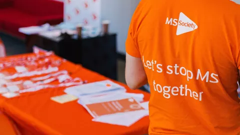 Back of someone's t-shirt reads 'Let's stop MS together', next to a table of MS Society branded publications