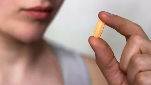 A woman holding a pill between her fingers