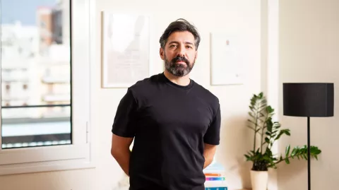 Periklis Papaloukas standing in a well-lit room, wearing a black t-shirt and looking at the camera