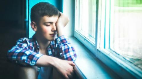 Image shows a young child crying and looking out of a window