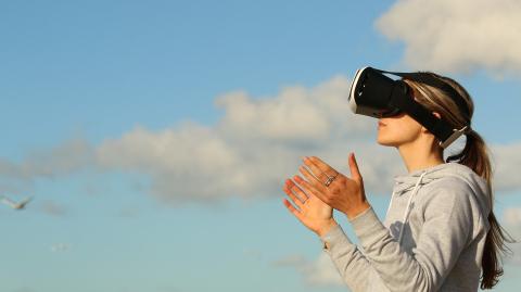 A woman wears a virtual reality headset with her hands out in front of her against a blue sky backround