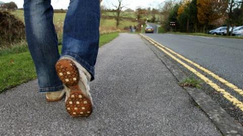 Photo of person's shoes walking on paved road