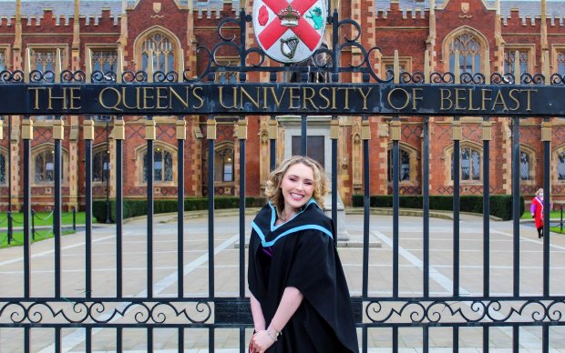 A photo of Anna in her graduation gown in front of The Queen's University of Belfast gates