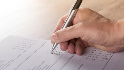 Close up of a hand filling in some forms with a pen